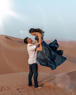 Romantic couple photoshoot by the best photographers in Dubai, with a man lifting a woman in a flowing dress on desert sand dunes.