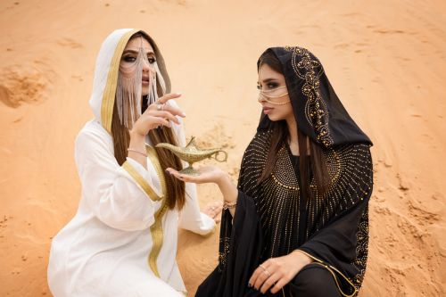 Top photographers in Dubai capturing two ladies in abayas with an Arabic lamp in the desert.