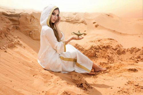 Top photographers in Dubai capturing a lady in white abaya sitting on desert sand dunes.